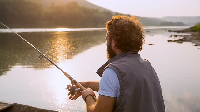 Curly man with a beard fishing on the river