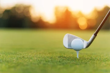 Foto auf Acrylglas Golf Der Golfschläger hinter dem Golfball auf dem Ständer. Vor dem Hintergrund von Gras und Sonnenuntergang