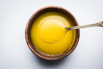 Ghee or clarified butter close up in wooden bowl and silver spoon, selective focus
