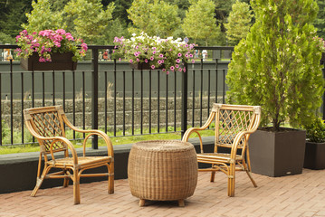 wicker outdoor furniture - two chairs and a round table - stand on the pedestrian promenade of a small river on a sunny day