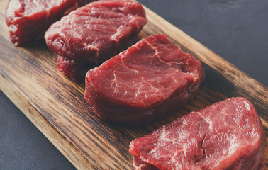 Raw beef filet mignon steaks on wooden board at gray background