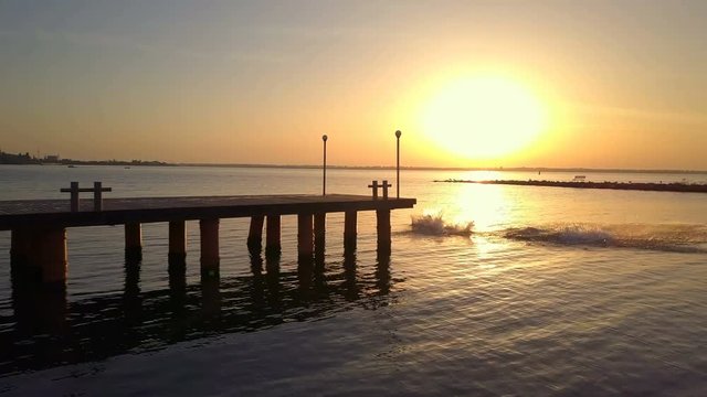 Silhouette friends running and jumping off sea pier sunset drone footage