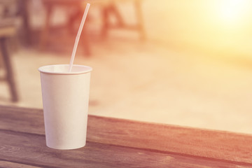 White paper cup of coffee on wooden table in garden