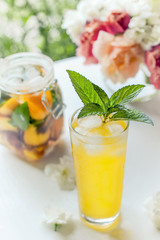 Transparent glass with water, detoxication with pieces of peach and apricot, with ice and mint close- up. A refreshing drink on the background of bouquet of pink peonies.