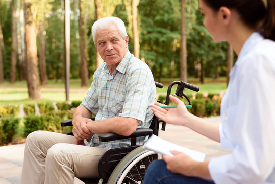 An elderly man in a wheelchair at a doctor's reception in a summer park