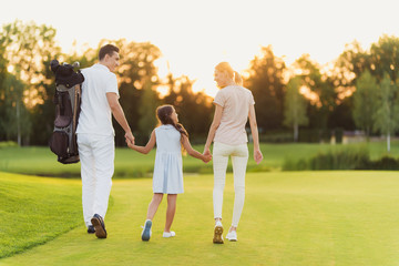 The family is walking along the golf course. Mother and father holding hands of their daughter