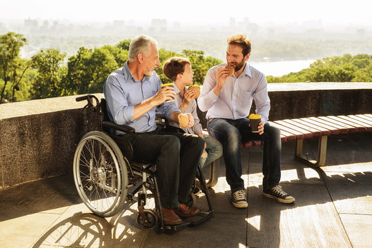 The old man in a wheelchair, his son and his grandson eat in the park