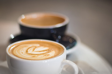 two cups of coffee in cafe, white one with heart shape latte art, black one with beautiful bokeh as background, 