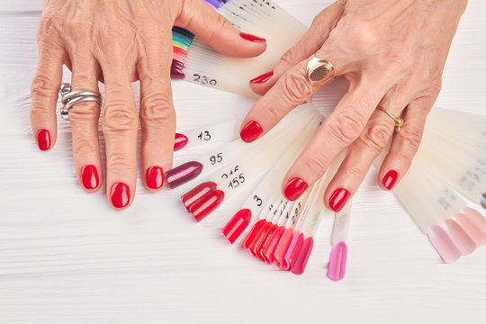 Senior woman hands with red manicure. Old woman well-groomed hands wearing rings. Female manicured hands and nails color samples.
