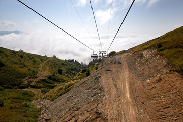 Naklejka premium View from top of ropeway with multiple seats and stretched cables above trees in deep fog. Mountains of the North Caucasus.
