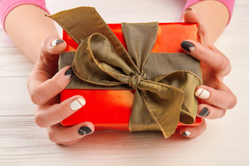 Gift box in female manicured hands. Woman hands with black and white manicure holding red box with gift. Holidays and celebrations concept.