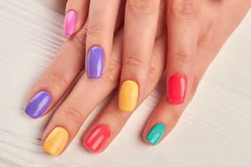Female fingers with colorful nails. Beautiful woman hands with pastel colors nails on white wooden background. Well-groomed hands with summer manicure.