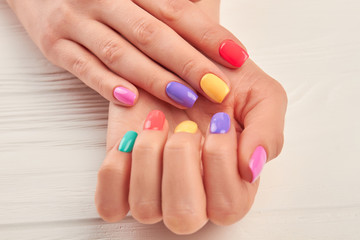 Female hands with stylish summer manicure. Woman hands with colorful nail polish close up. Well-groomed hands with bright manicure on wooden background.