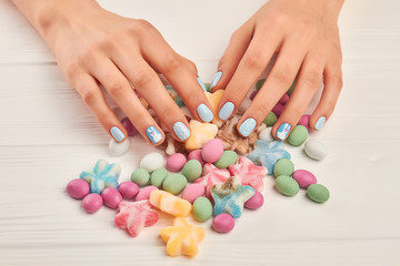 Woman manicured hands and sweets. Female hands with beautiful winter manicure and many colorful candies close up. Creative winter nails design.