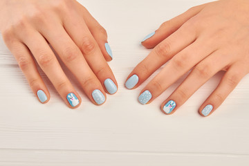 Winter design manicure on female hands. Well-groomed woman hands with gentle manicure. Young woman manicured hands on white wooden background.