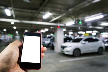 hand using mobile smart phone with blurred image of indoor car parking garage area, RFID solution management system, internet, social media and car parking sensor technology concept