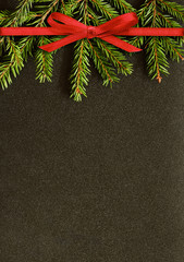 Black Christmas background with fir-tree twigs and red ribbon bow