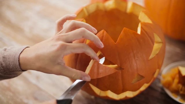 close up of woman carving halloween pumpkin