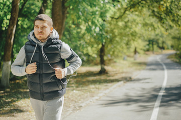 young active male runner in a tracksuit and jumper with headphones. Training for health in the park in the fall.