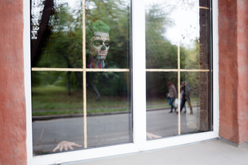 View of man with skeleton make up in the window. Halloween makeup concept, scary man in window.