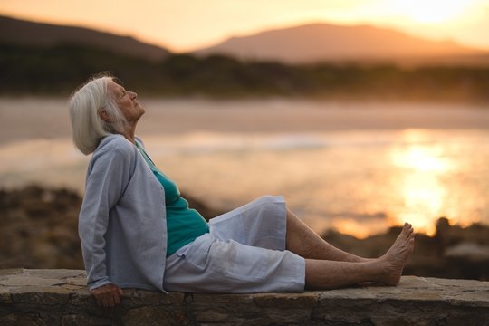Senior Woman Relaxing On Wall At Beach
