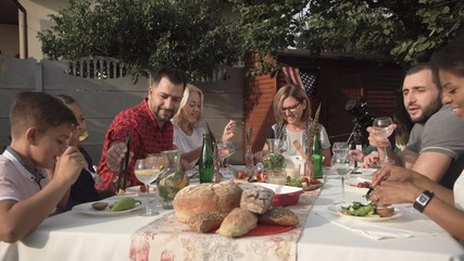 Middle angle of cheerful big American family sitting and eating in the garden during reunion party.