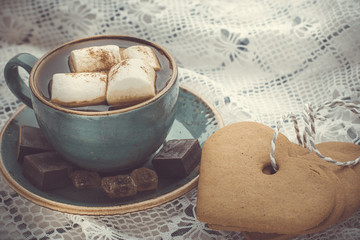 Christmas concept. Blue mug of hot coffee with marshmallow on a white lace with cookies. Toned image.