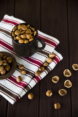 hazelnuts in a clay mug with shell around on a wooden table and striped towel