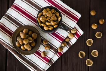 hazelnuts in a clay mug with shell around on a wooden table and striped towel