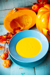 Pumpkin soup with cream, cheese and pumpkin seeds on blue wooden background. Pumpkin soup with fresh pumpkins. Halloween Thanksgiving Autumn food concept. Top view.