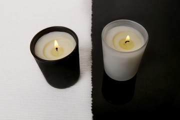 Fototapeta na wymiar White and black candles. Two burning candles on black table with white napkin.