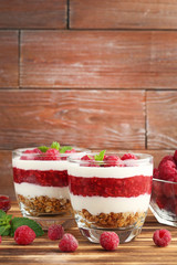 Dessert with raspberries and granola in glasses on brown wooden table