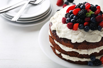Delicious chocolate biscuit cake with berries on white wooden table