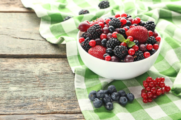 Ripe and sweet berries in bowl on wooden table