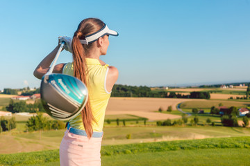 Young woman holding a driver club behind her back during golf swing, at the beginning of a...