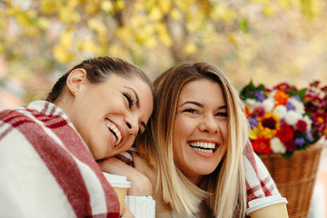 Obraz premium Two women smiling and laughing with a blanket on a bench enjoying coffee