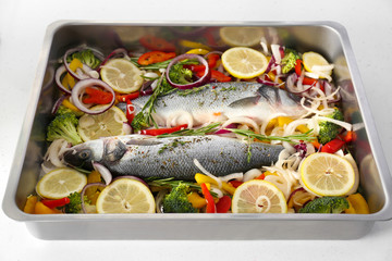 Baking tray with uncooked fish and vegetables on white background