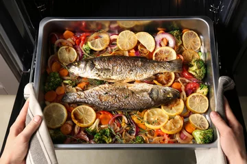 Photo sur Plexiglas Poisson Femme prenant une plaque de cuisson avec du poisson et des légumes hors du four