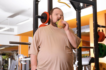 Fototapeta na wymiar Overweight man eating sandwich in gym