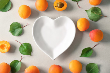 Fresh apricots around plate in shape of heart on light background