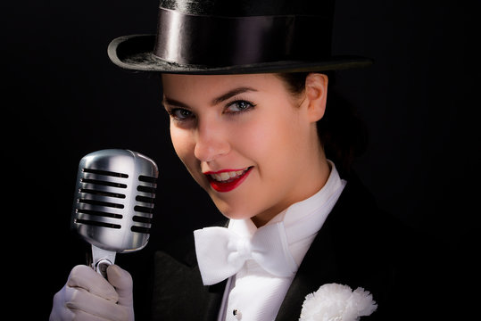 Beautiful young woman dressed in vintage top hat and tails with old microphone. 

