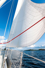 Fototapeta premium White yacht sails in sunlight on blue cloudy sky background.