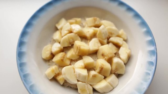 Healthy breakfast, oatmeal porridge with milk and banana. Oat flakes filled with milk in a faience dish on a white background. Organic food concept for good health.