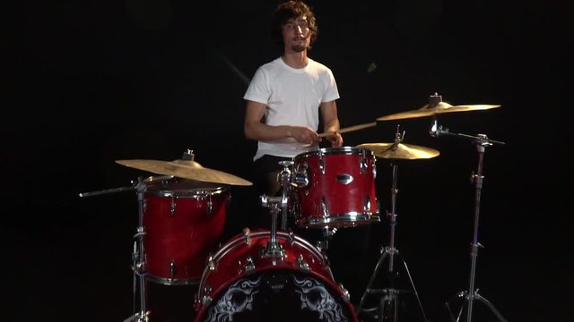 In slow motion, a drummer with curly hair plays drum sticks on drums