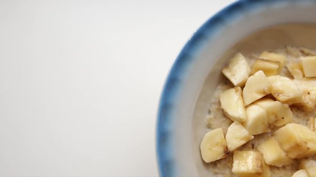 Creative food background. Healthy breakfast, oatmeal porridge with milk and fresh bananas. Oat flakes filled with milk in a faience dish on a white background. Organic food for good health.
