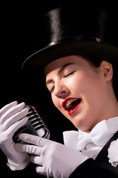 Beautiful young woman dressed in vintage top hat and tails with old microphone.