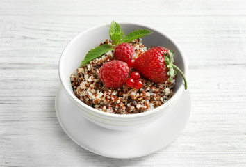 Tasty quinoa with berries in bowl on wooden table