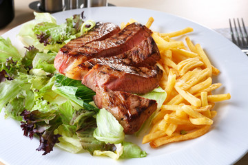Plate with delicious steak and garnish on table in cafe