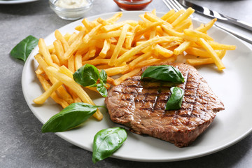 Plate with delicious steak and fries on table in cafe