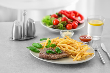Plate with delicious steak and fries on table in cafe